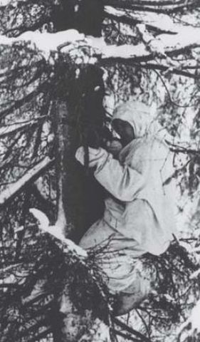 Explorador de la guerrilla subido a un árbol. Va equipado con botas valenki de fieltro y uniforme de camuflaje